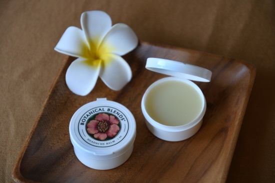 1 oz headache balm containers on wood plate with white tropical flower