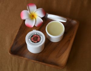 2 oz headache balm containers on wood plate with tropical flower