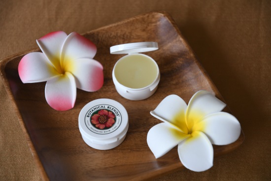 0.5 oz size of headache balm on wooden tray with tropical flowers